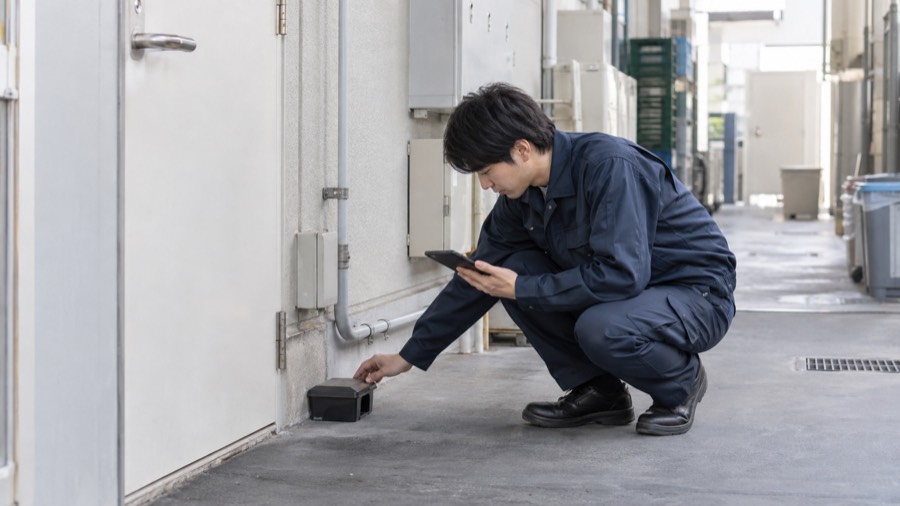 施設の裏口でトラップを確認する防除作業員